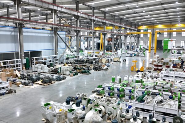 Wide pellet equipment workshop showing production areas, machines, parts, cranes, and staff