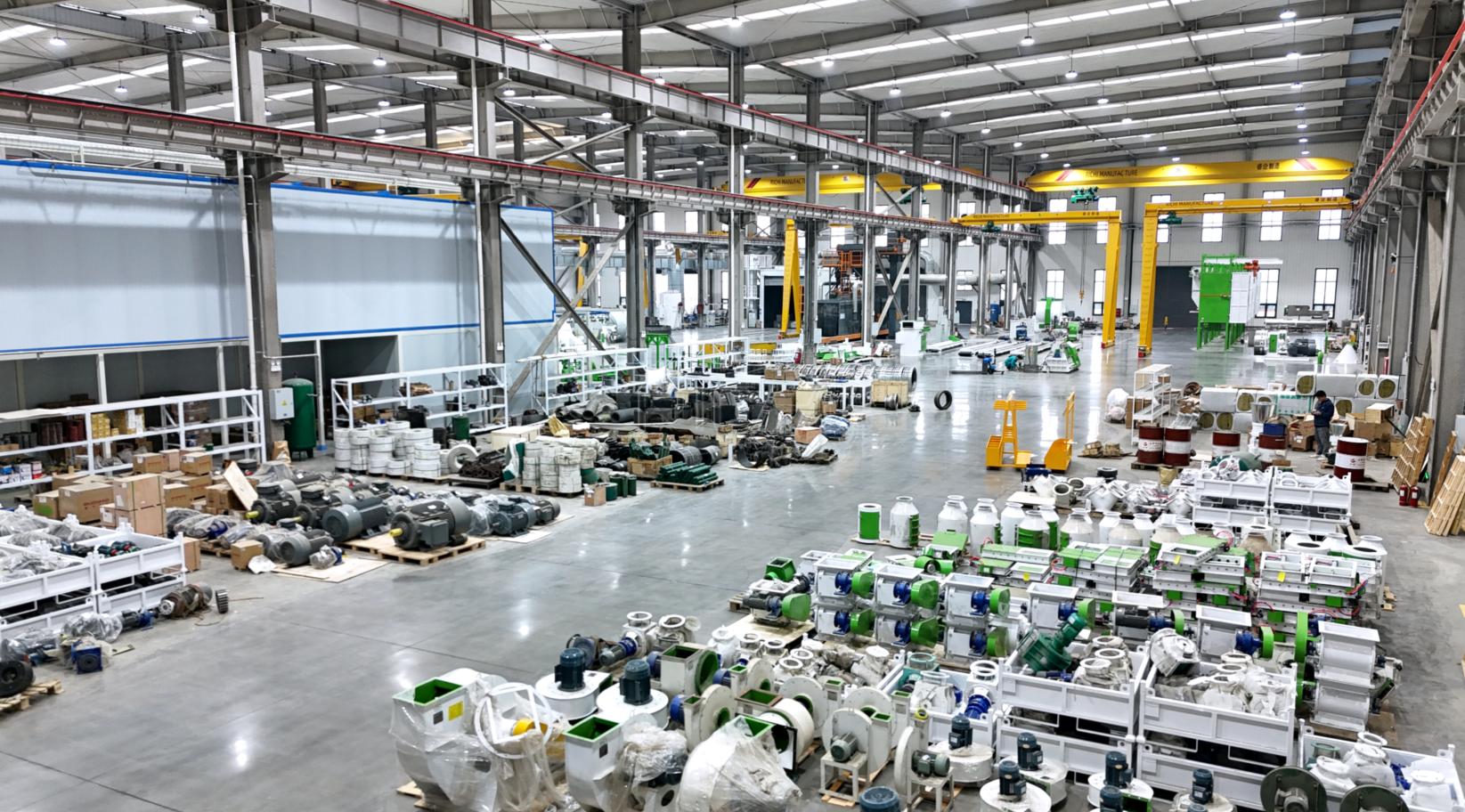 Wide pellet equipment workshop showing production areas, machines, parts, cranes, and staff
